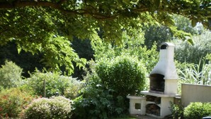 Un jardin agrémenté d’un barbecue en pierre, entouré d’une végétation luxuriante et d’une pelouse.