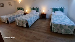 Une chambre avec trois lits simples, chacun doté d’une table de chevet et d’une lampe, et une lucarne au plafond.