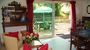 A living room with a sofa, a dining table, and a patio area with a table and chairs. - Cozy Traditional Cottage with Private Garden, Near La Garnache (La Garnache)