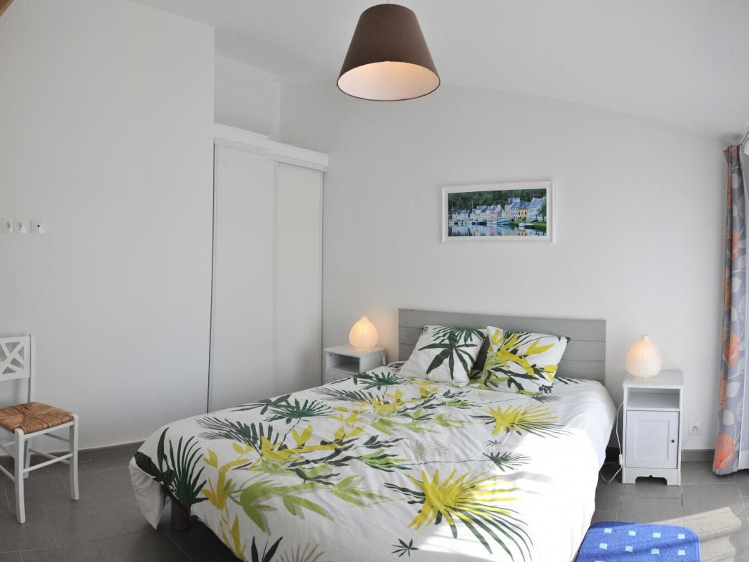 Une chambre à coucher avec un lit, deux tables de chevet, une chaise, une lampe suspendue et un tableau au mur.