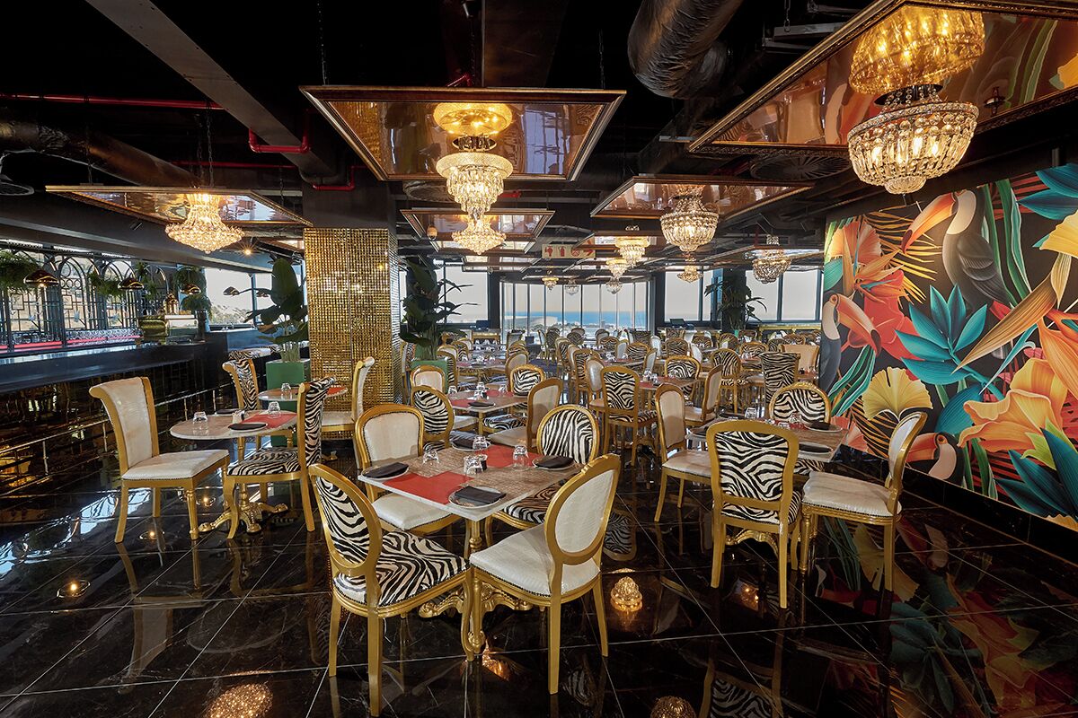 A restaurant with zebra-striped chairs, chandeliers, and a tropical mural.