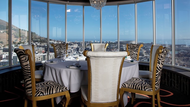A dining area with a panoramic city view, featuring zebra-striped chairs and a chandelier. - Hotel Sky Cape Town (Cape Town)
