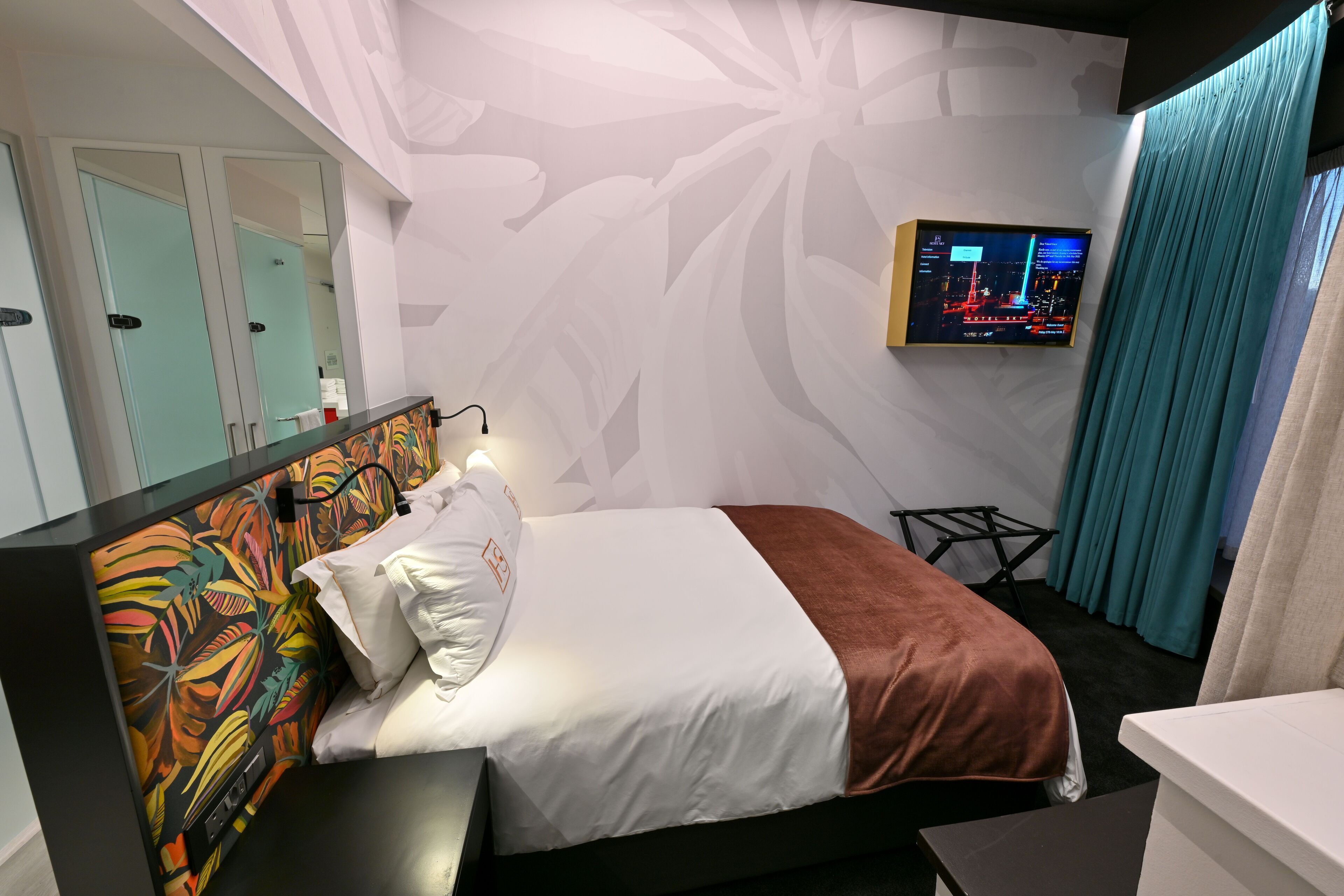 Une chambre d’hôtel avec un lit, un téléviseur fixé au mur et un miroir.