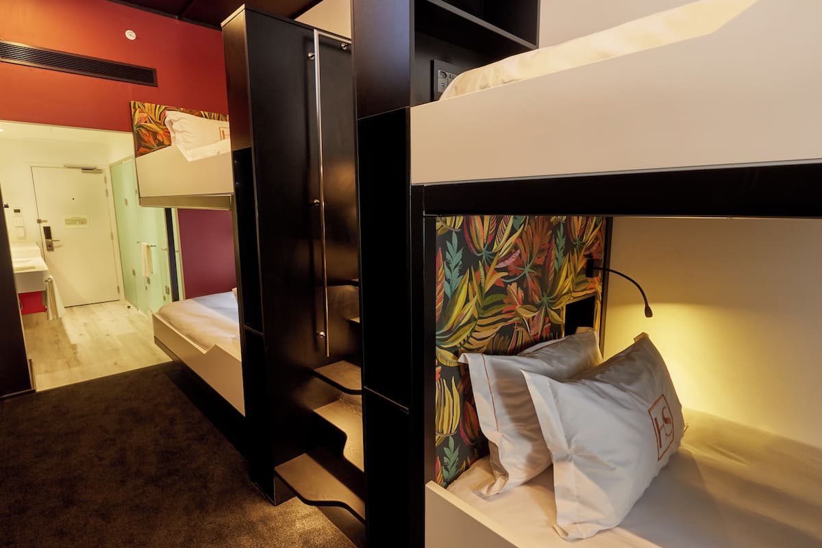 A bunk bed room with a colorful headboard, a white pillow, and a visible door leading to another room.
