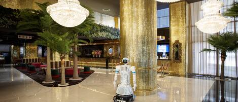 Un hall d’entrée avec un robot, des lustres, une colonne dorée et un espace d’accueil.