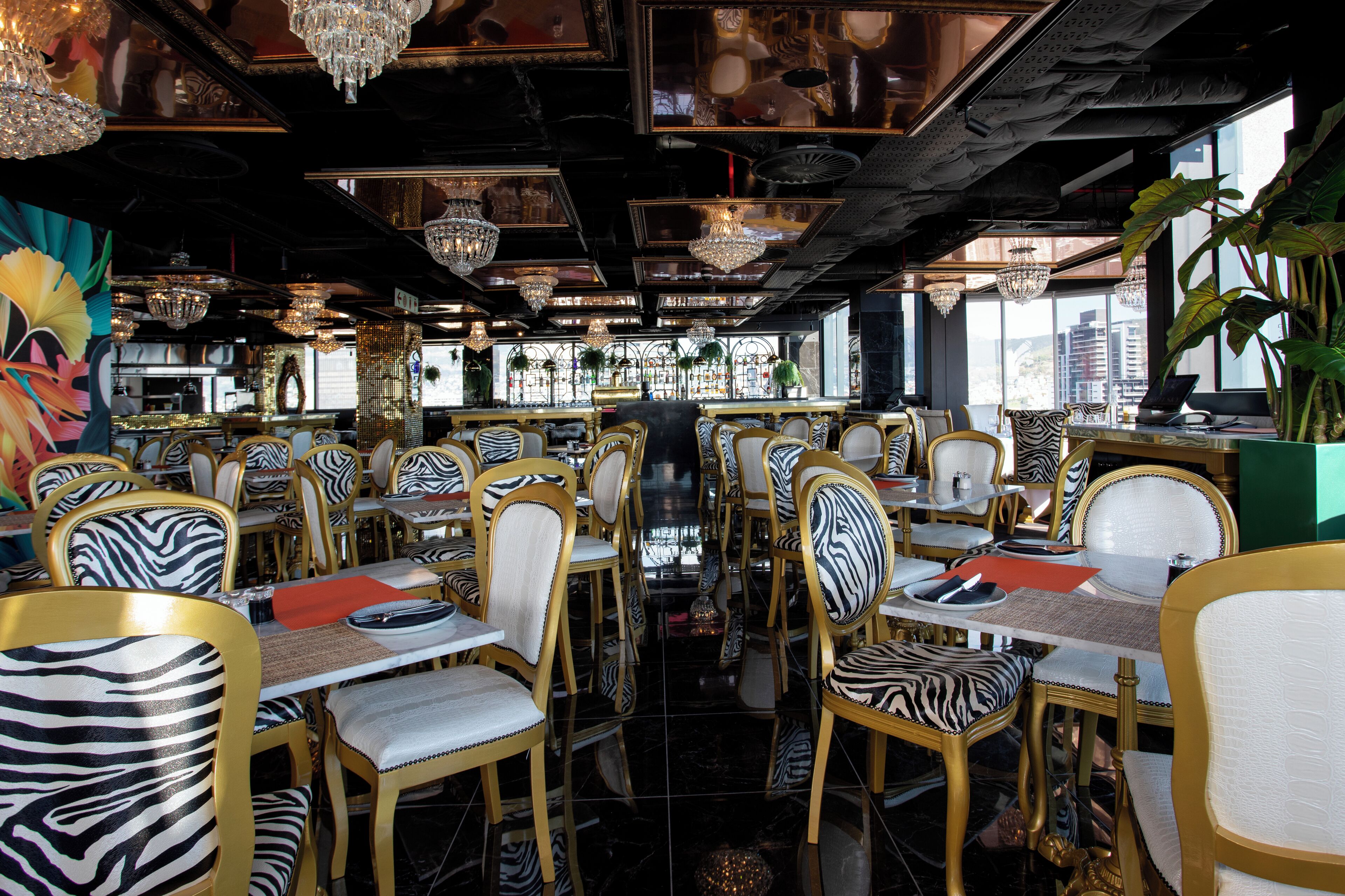 Een restaurant met streepstoelen, kroonluchters en uitzicht op de stad.