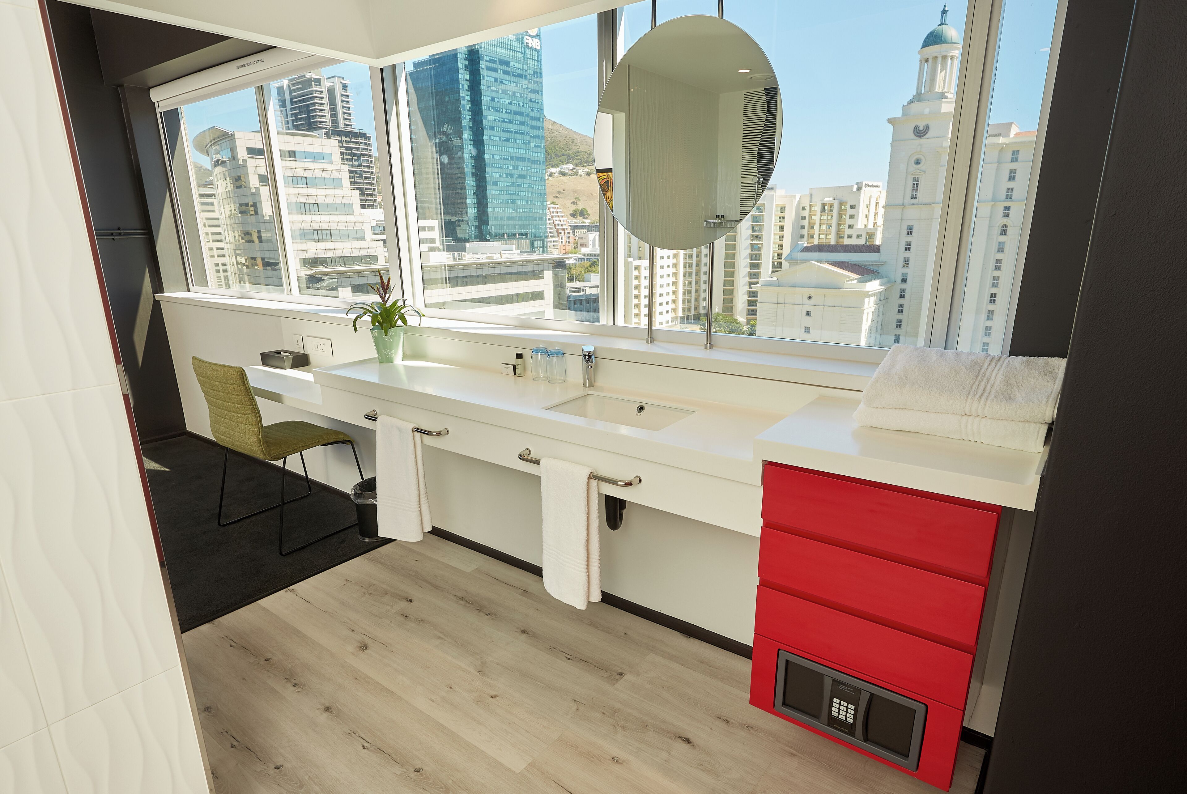 Een moderne badkamer met een groot raam, een wastafel, een spiegel en een rode kast.