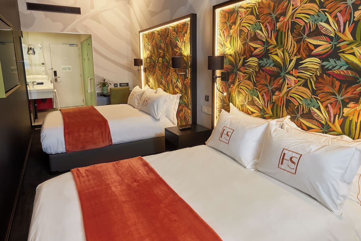 A hotel room with two beds, a large floral wall mural, a mirror, and a bathroom visible through an open door.