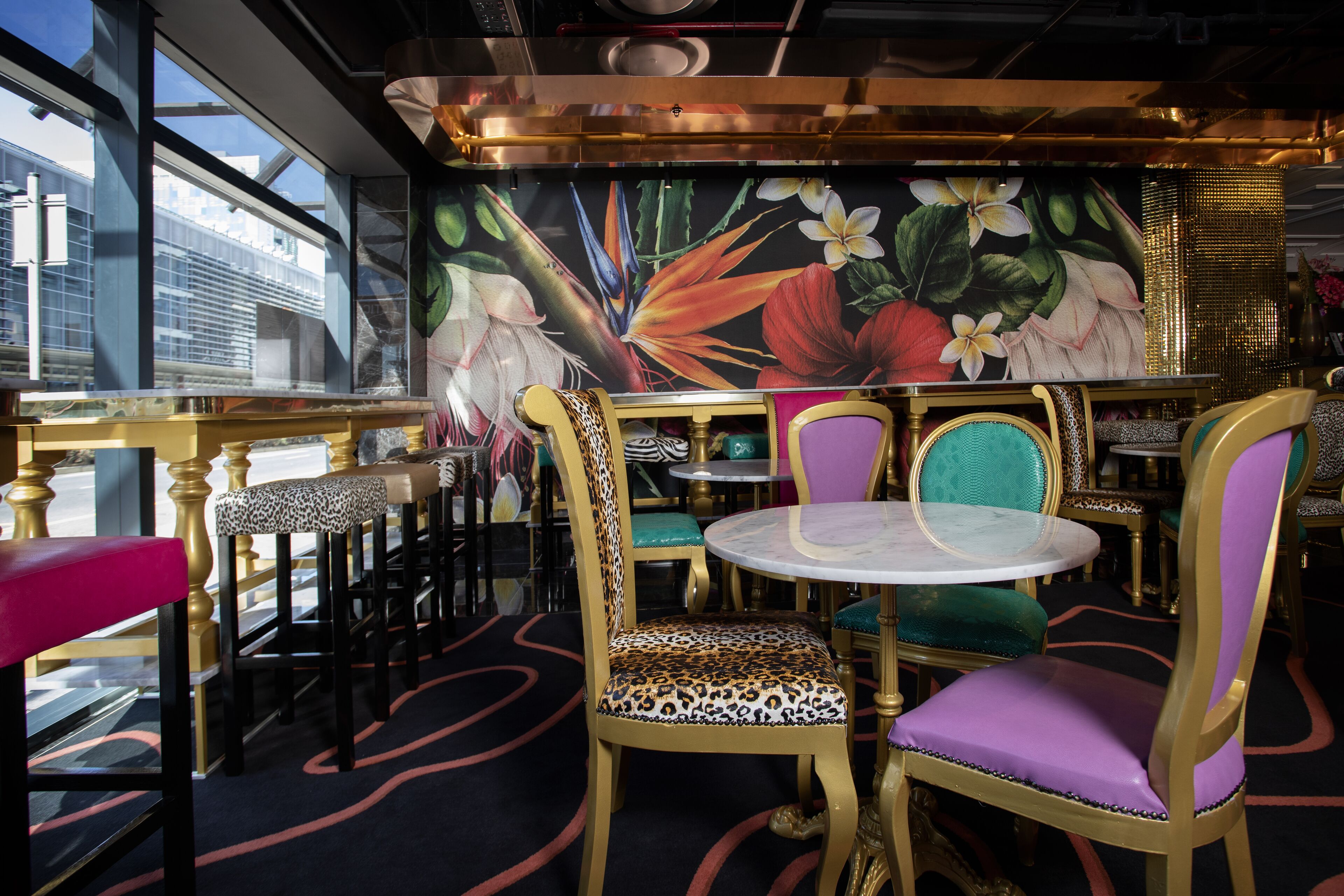 Un restaurant décoré d’une fresque murale aux motifs tropicaux, avec des chaises dorées et turquoise, et une table en marbre.