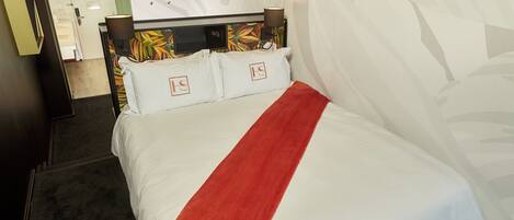 Una habitación de hotel con cama, cabecera con estampado floral, manta roja y pared con diseño de hojas.