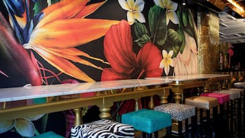 Un'area bar con un lungo bancone, diversi sgabelli con rivestimenti decorati e un grande murale floreale sulla parete.