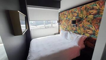 A hotel room with a bed, a window, and a colorful wall mural.