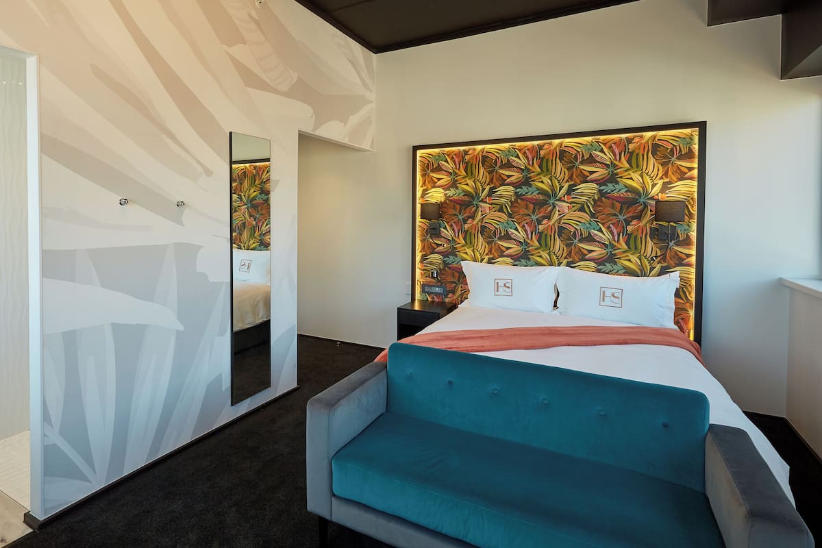 A modern hotel room with a large bed, a mirror, and a vibrant floral headboard.