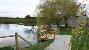 Un camí de grava que condueix a un moll de fusta sobre un llac tranquil, envoltat de verdura i una petita construcció de fusta.