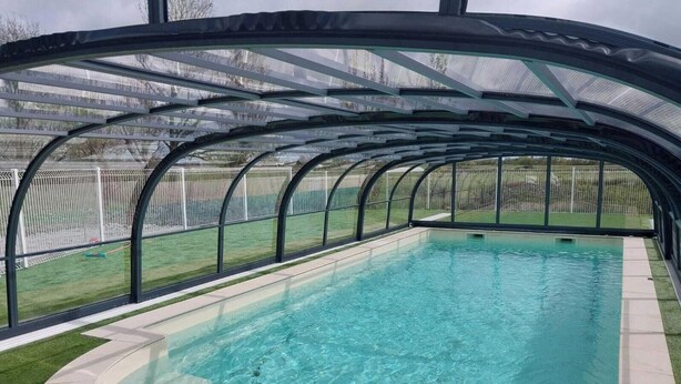 Una piscina amb zona coberta, envoltada per una tanca i una zona enjardinada.
