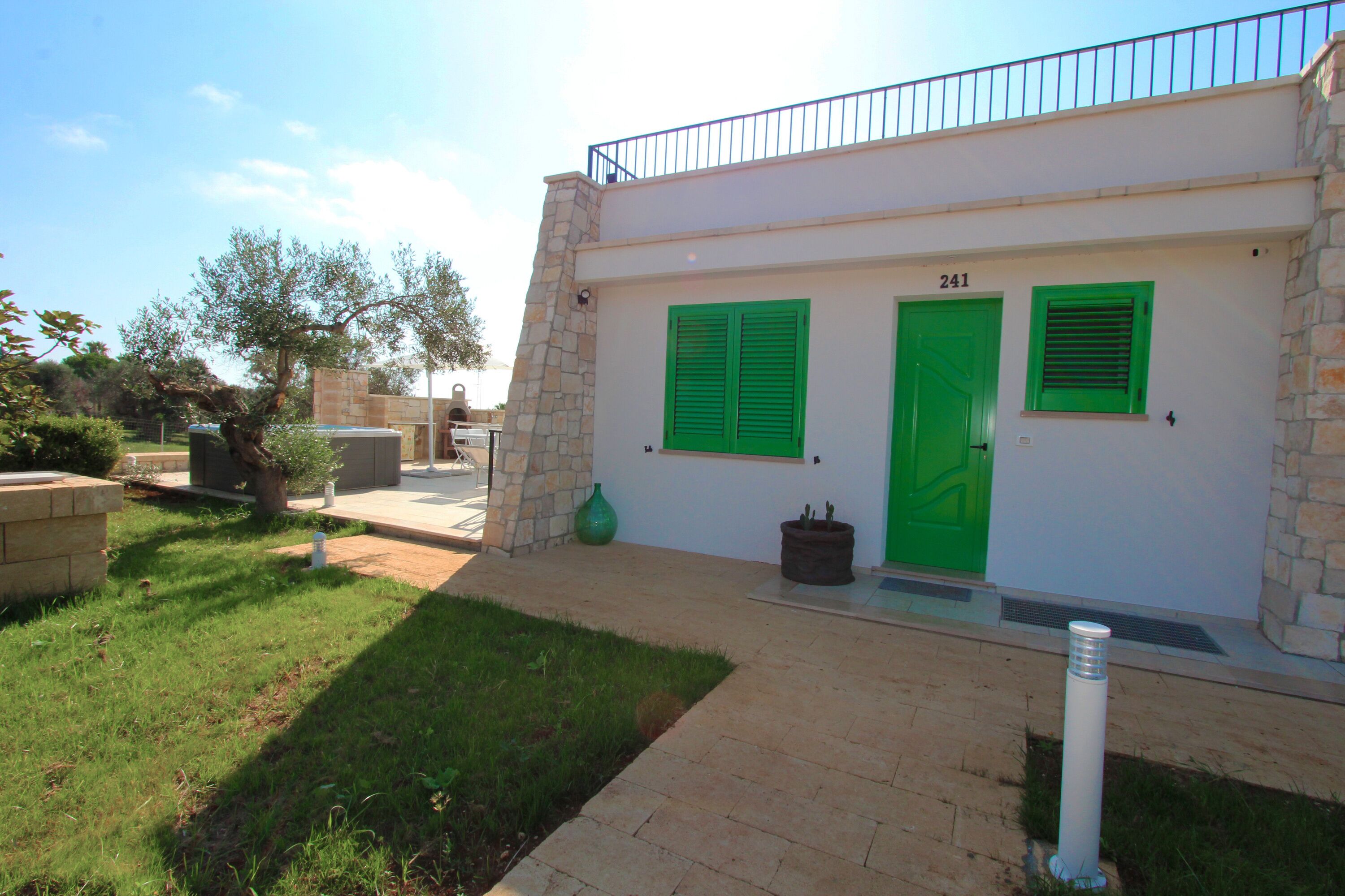 A building with a stone facade, numbered 241, featuring green shutters and a metal railing on the upper level.