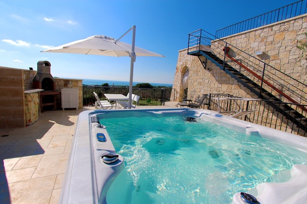 Una piscina con jacuzzi, un muro de piedra y vista al mar.