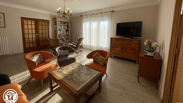 A living room with a wooden coffee table, two armchairs, a sofa, a bookshelf, a television, and a decorative vase.