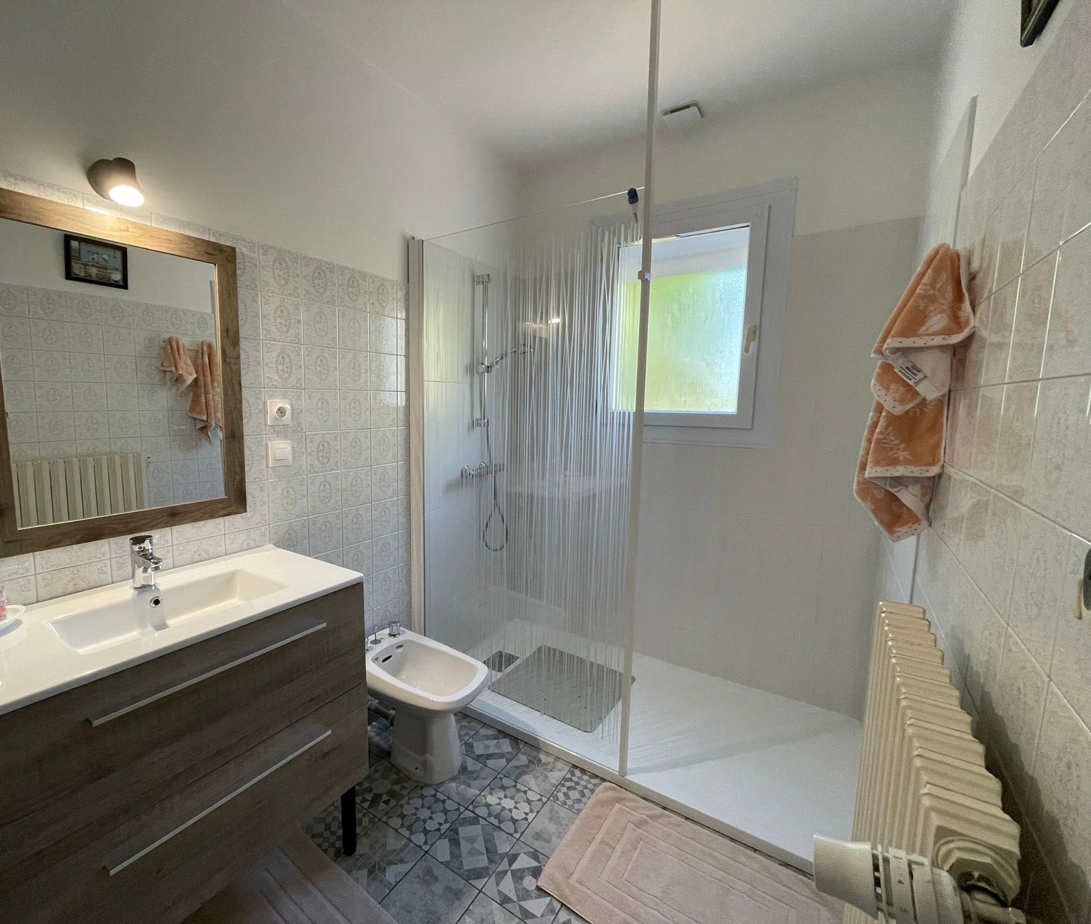 A modern bathroom with a large mirror, a sink, a bidet, and a shower enclosure.