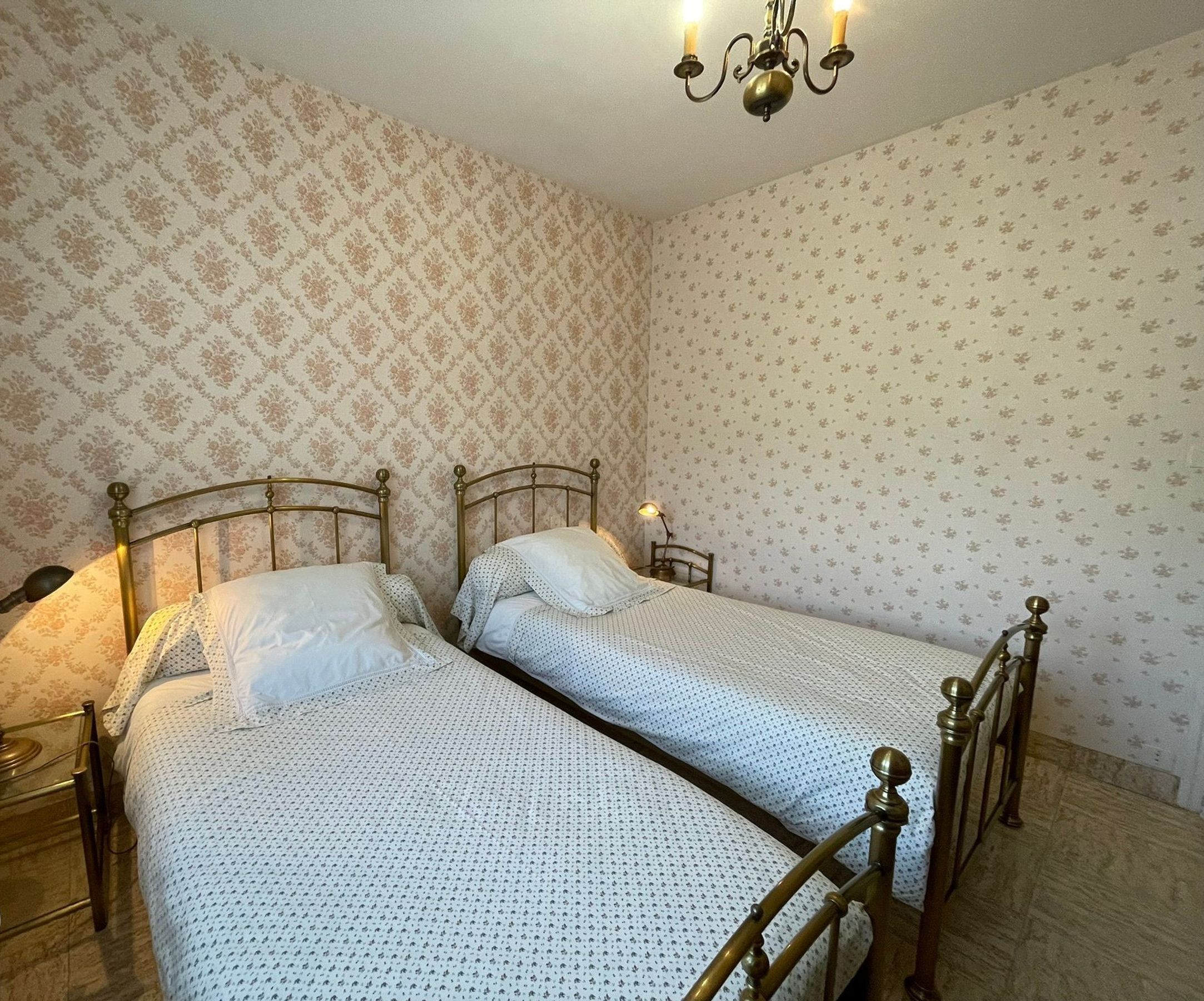 Ein Schlafzimmer mit zwei Einzelbetten, einem Chandelier und Wandtapete mit Muster.