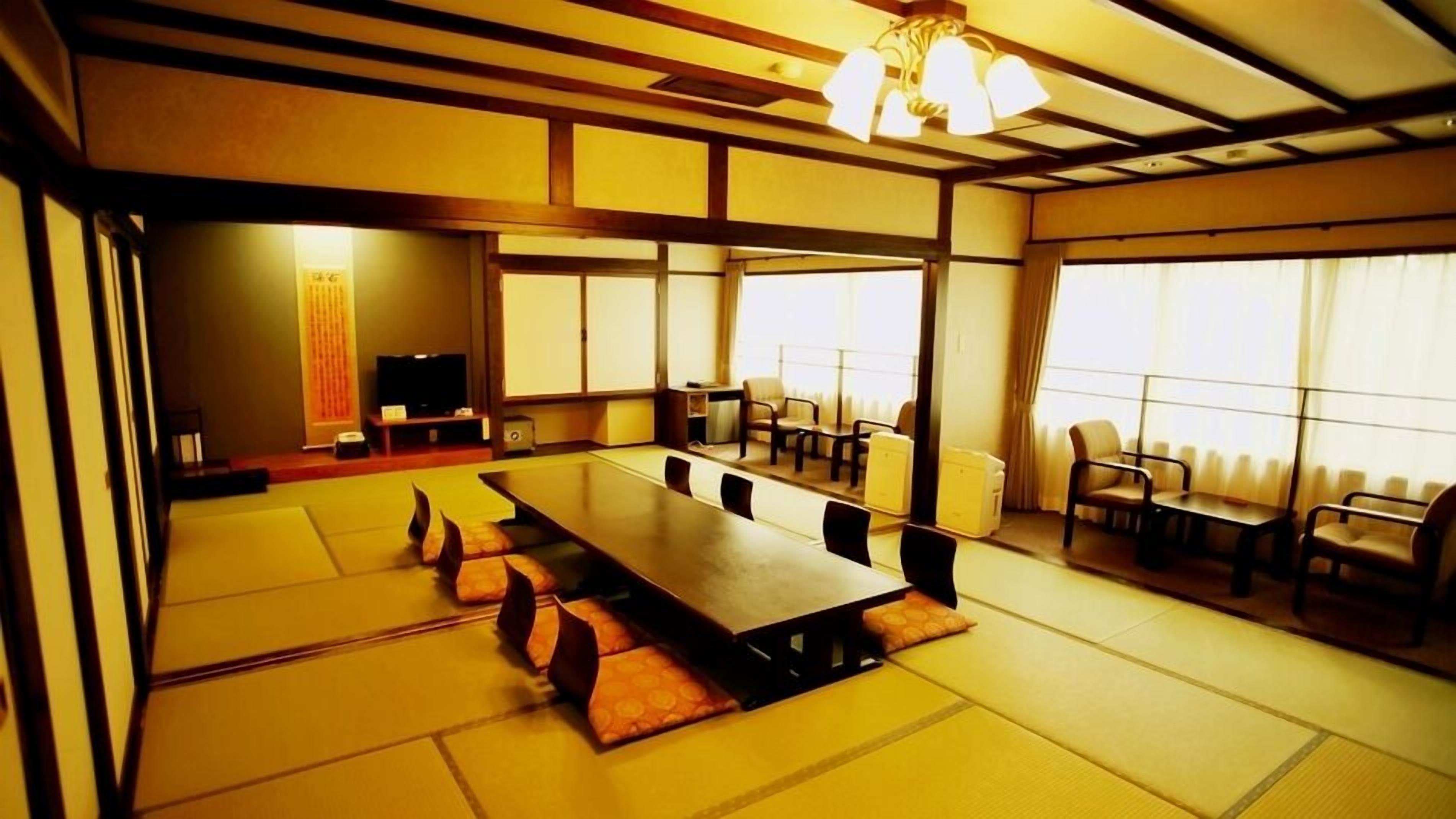A traditional Japanese-style room with tatami flooring, a long table, and chairs.
