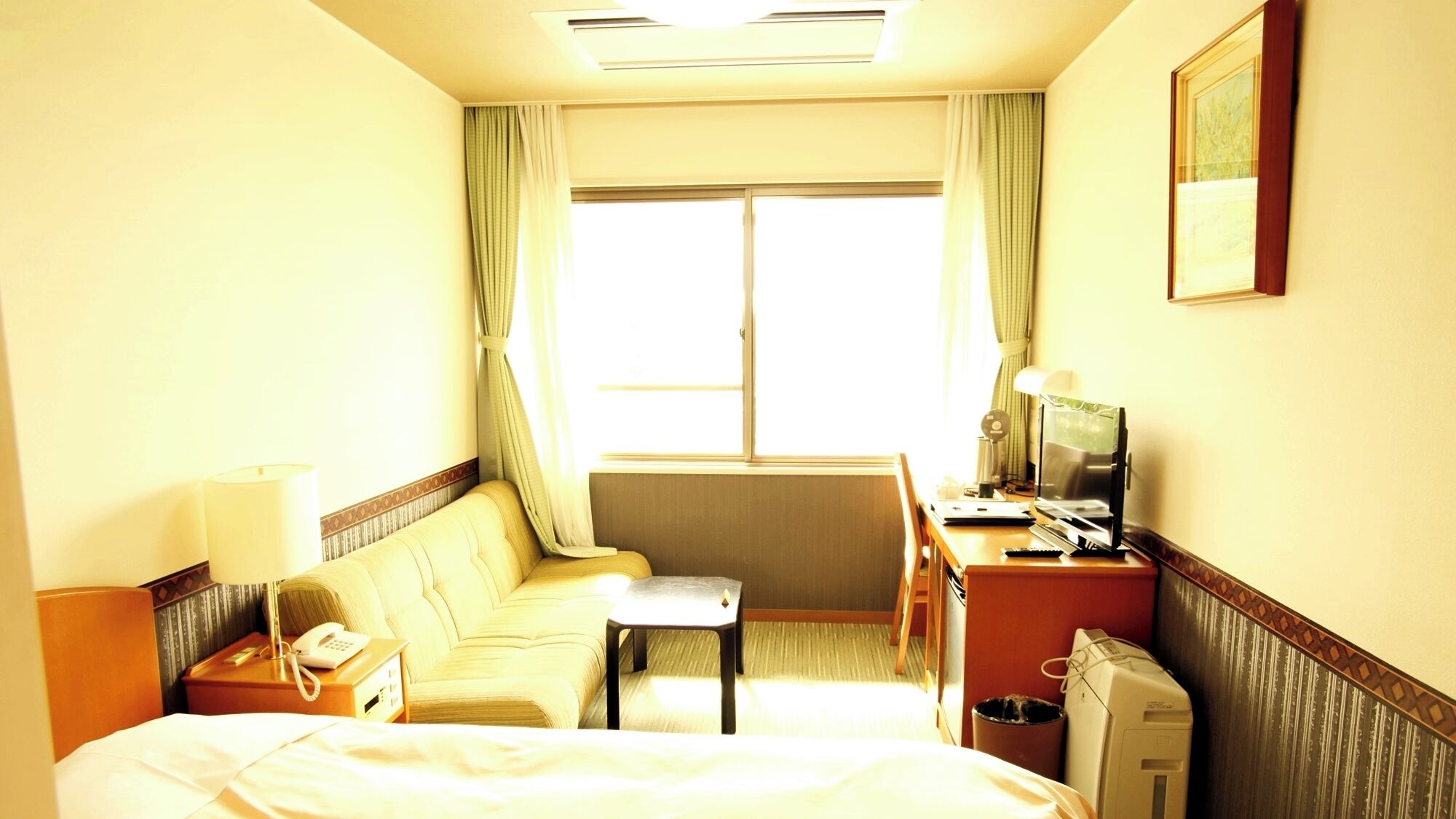Habitación de hotel con cama, sofá, escritorio con computadora, teléfono y ventana con cortinas.