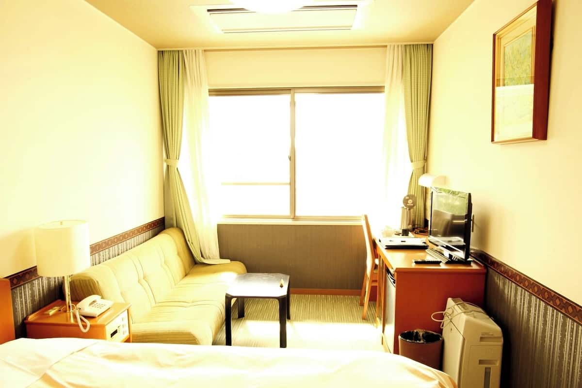 Habitación de hotel con cama, sofá, escritorio con computadora, teléfono y ventana con cortinas.