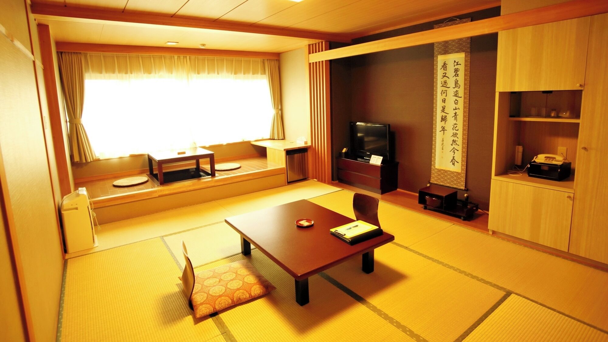 Una habitación tradicional japonesa con suelo de tatami, una mesa baja, un televisor y un mueble con un pergamino decorativo.