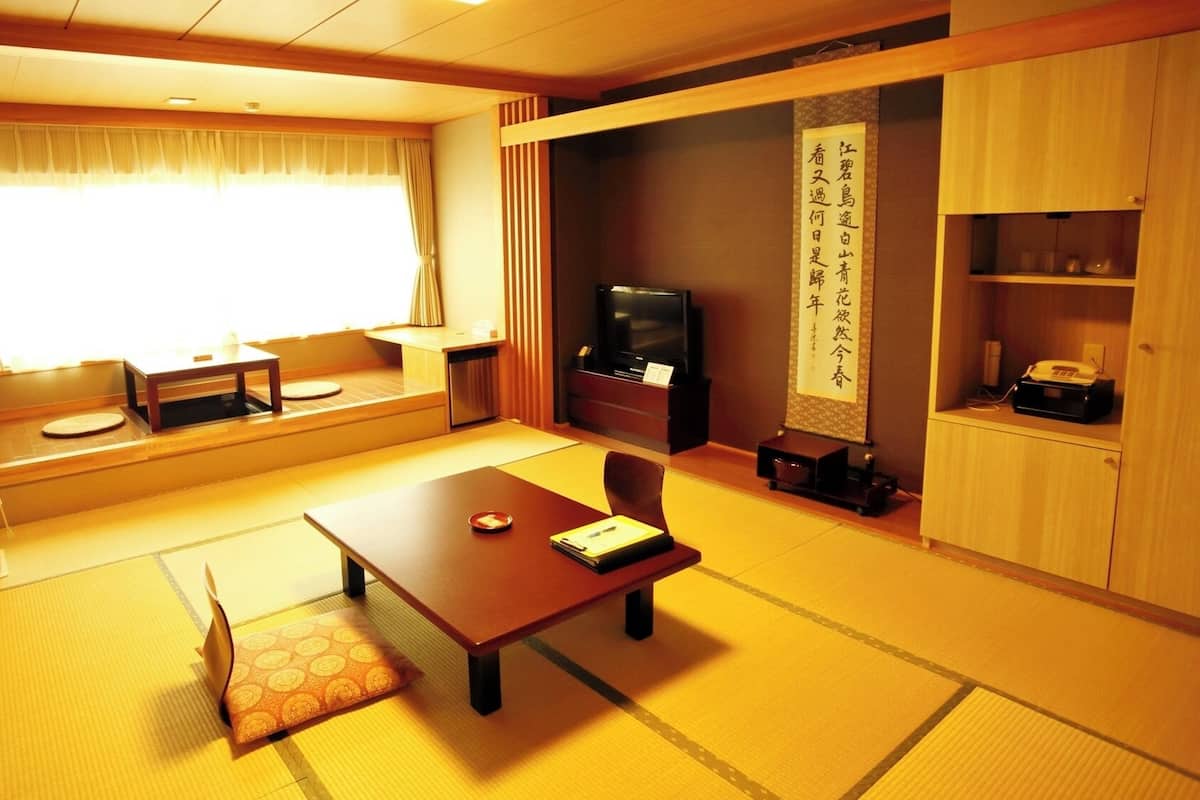 Una habitación tradicional japonesa con suelo de tatami, una mesa baja, un televisor y un mueble con un pergamino decorativo.