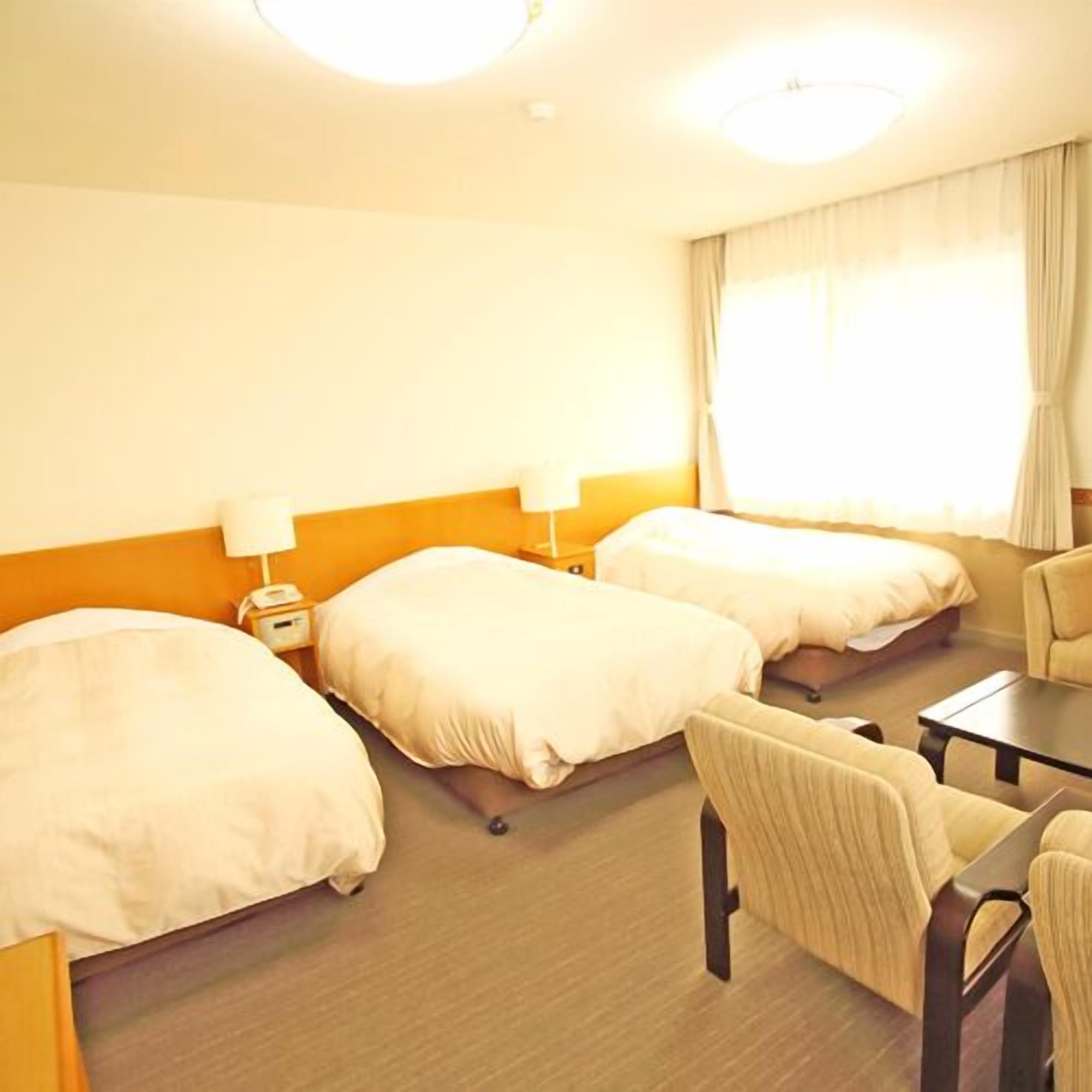 A hotel room with two beds, a desk, a chair, and a window with curtains.