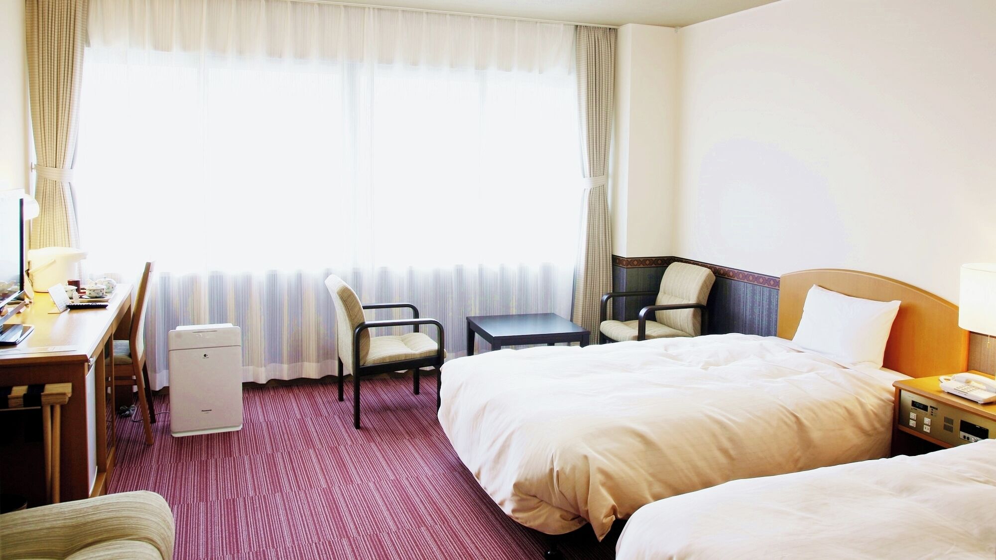 Habitación de hotel con dos camas, un escritorio, una silla, una mesita y un radiador.
