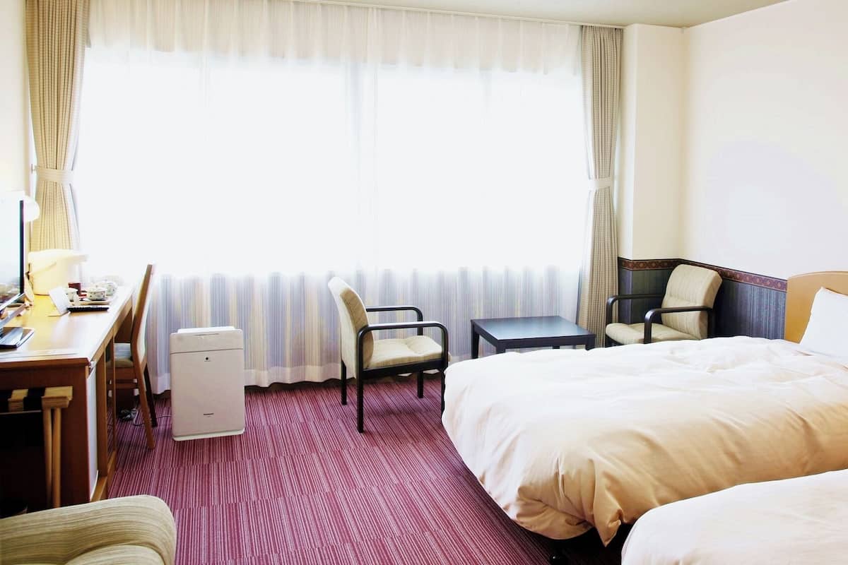 Habitación de hotel con dos camas, un escritorio, una silla, una mesita y un radiador.