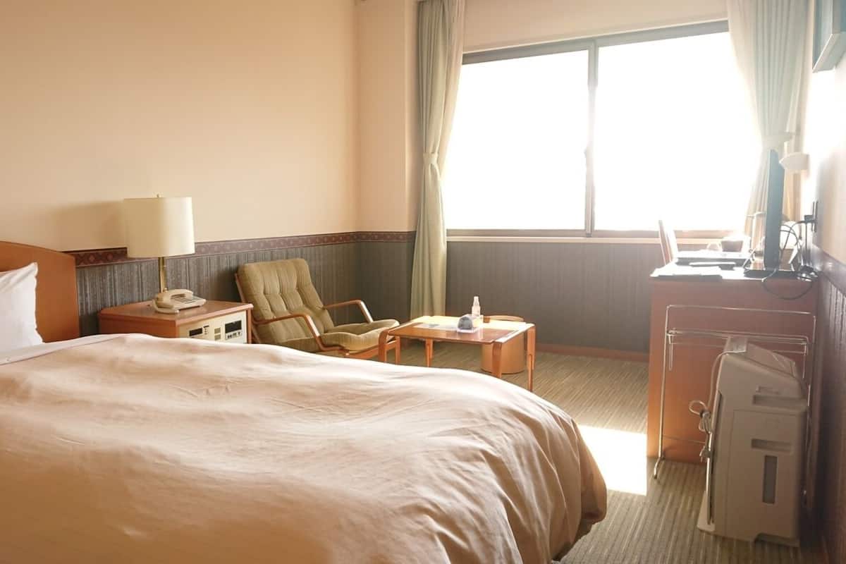 Habitación de hotel con una cama grande, una silla, un escritorio con lámpara y una ventana con cortinas.
