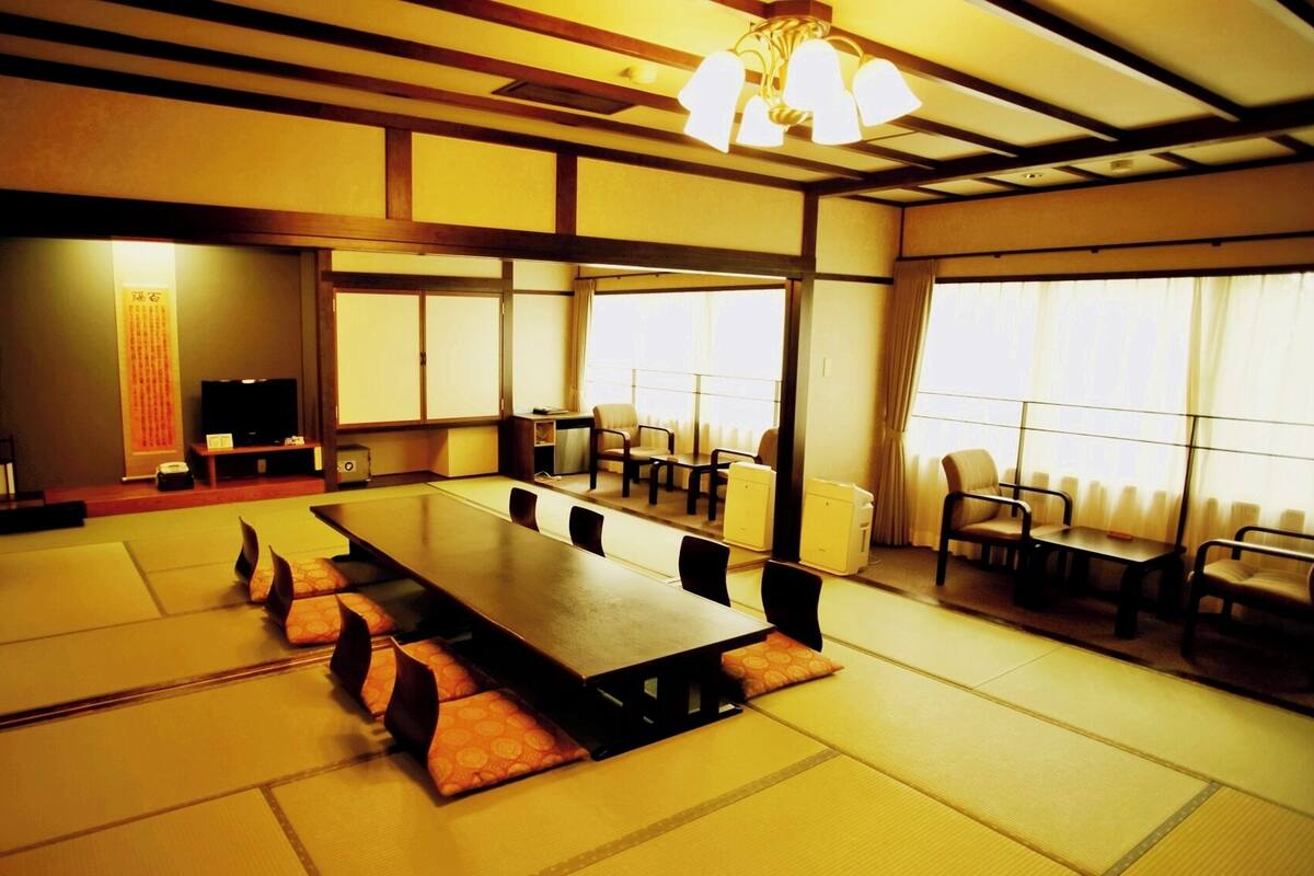 Una habitación de estilo japonés tradicional con suelo de tatami, una mesa larga y varias sillas.