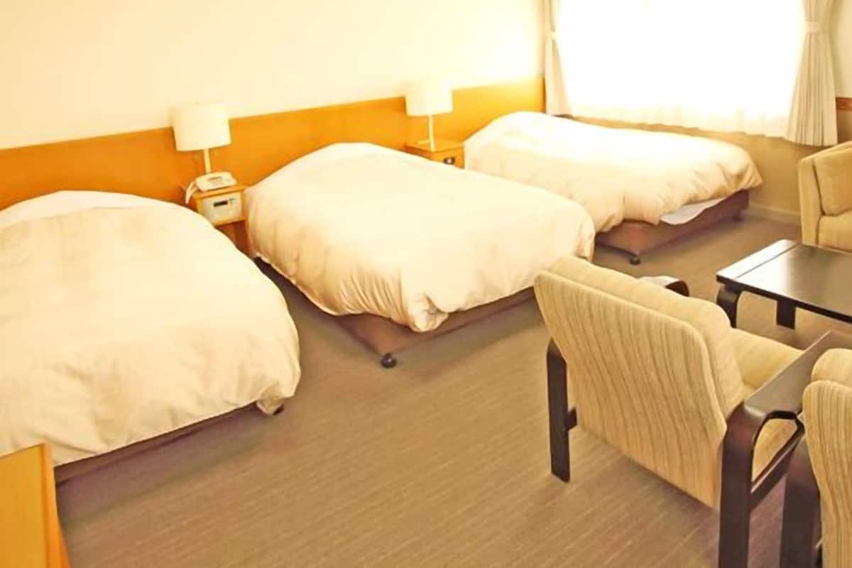 Una habitación de hotel con dos camas, un escritorio, una silla y un ventanal con cortinas.