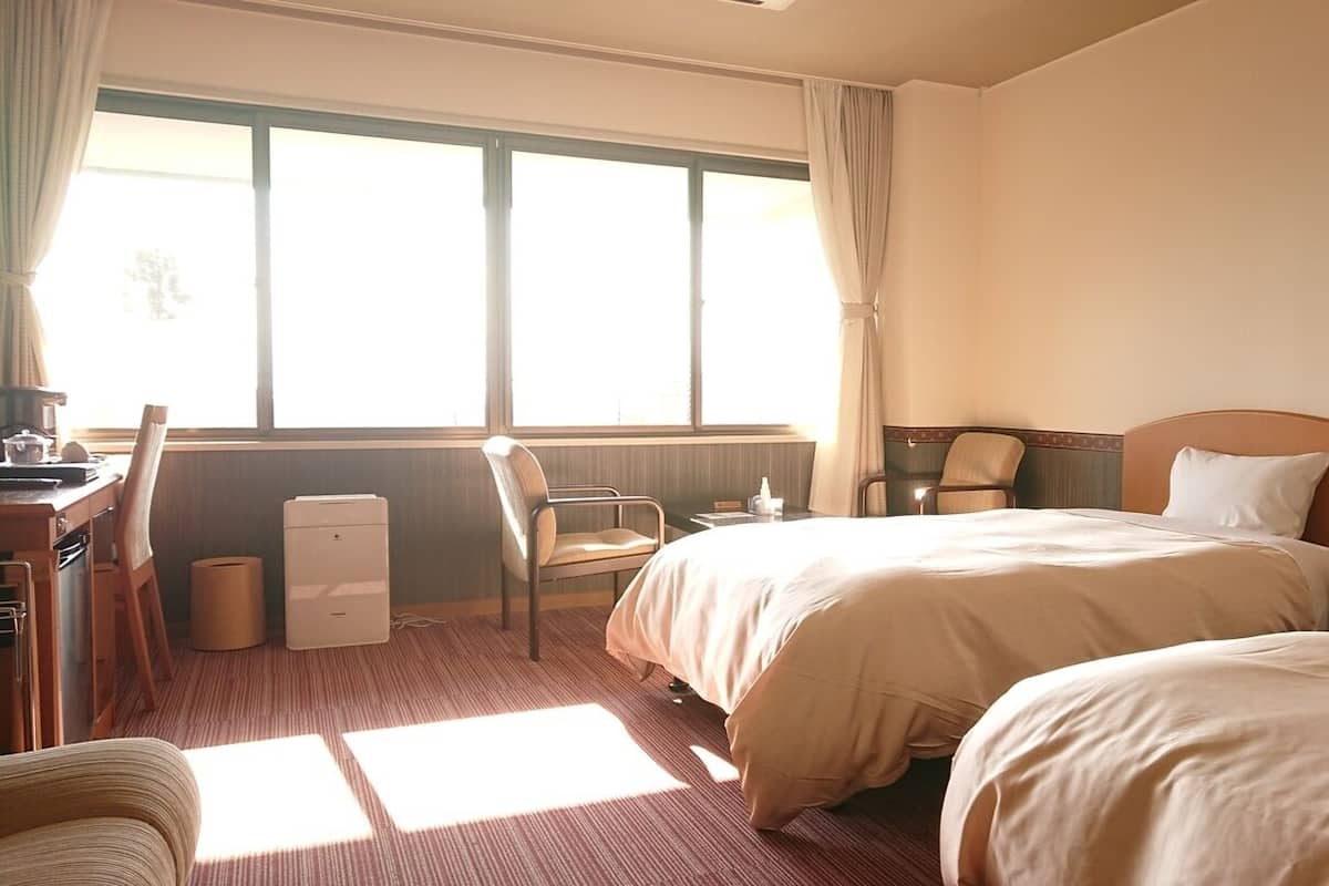 Habitación de hotel con dos camas, un escritorio, una silla, una lámpara y una ventana.