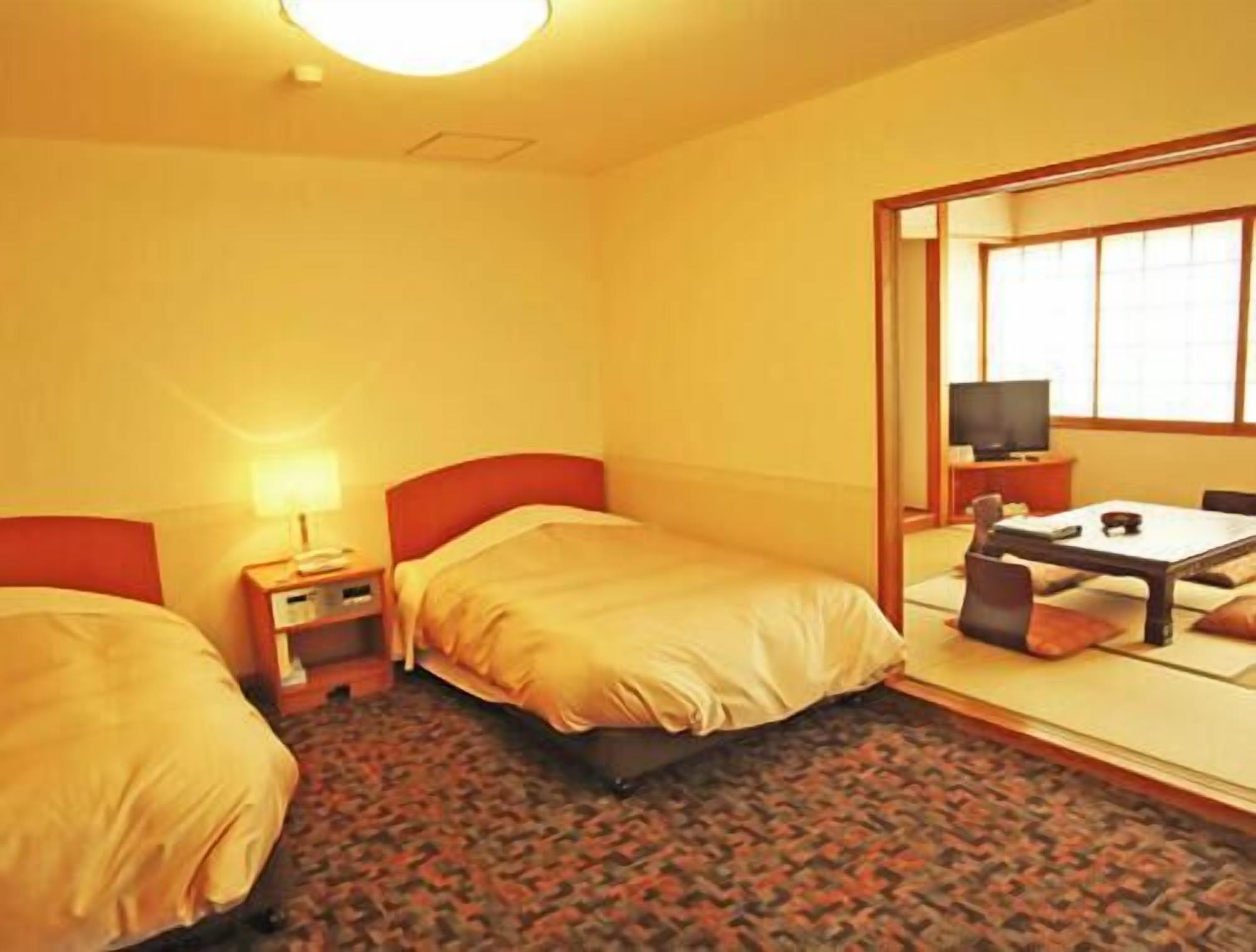 Habitación de hotel con dos camas, un escritorio con silla, un televisor y un espejo grande.