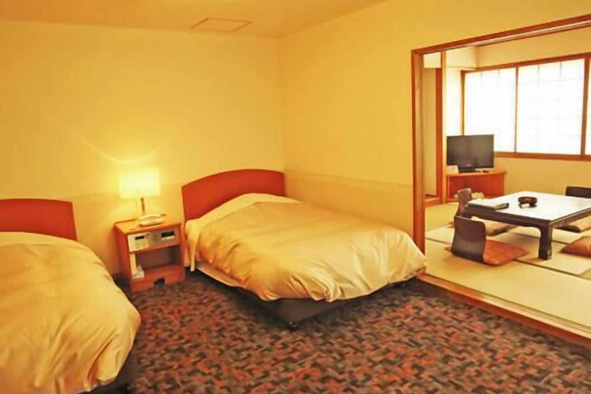 Habitación de hotel con dos camas, un escritorio con silla, un televisor y un espejo grande.