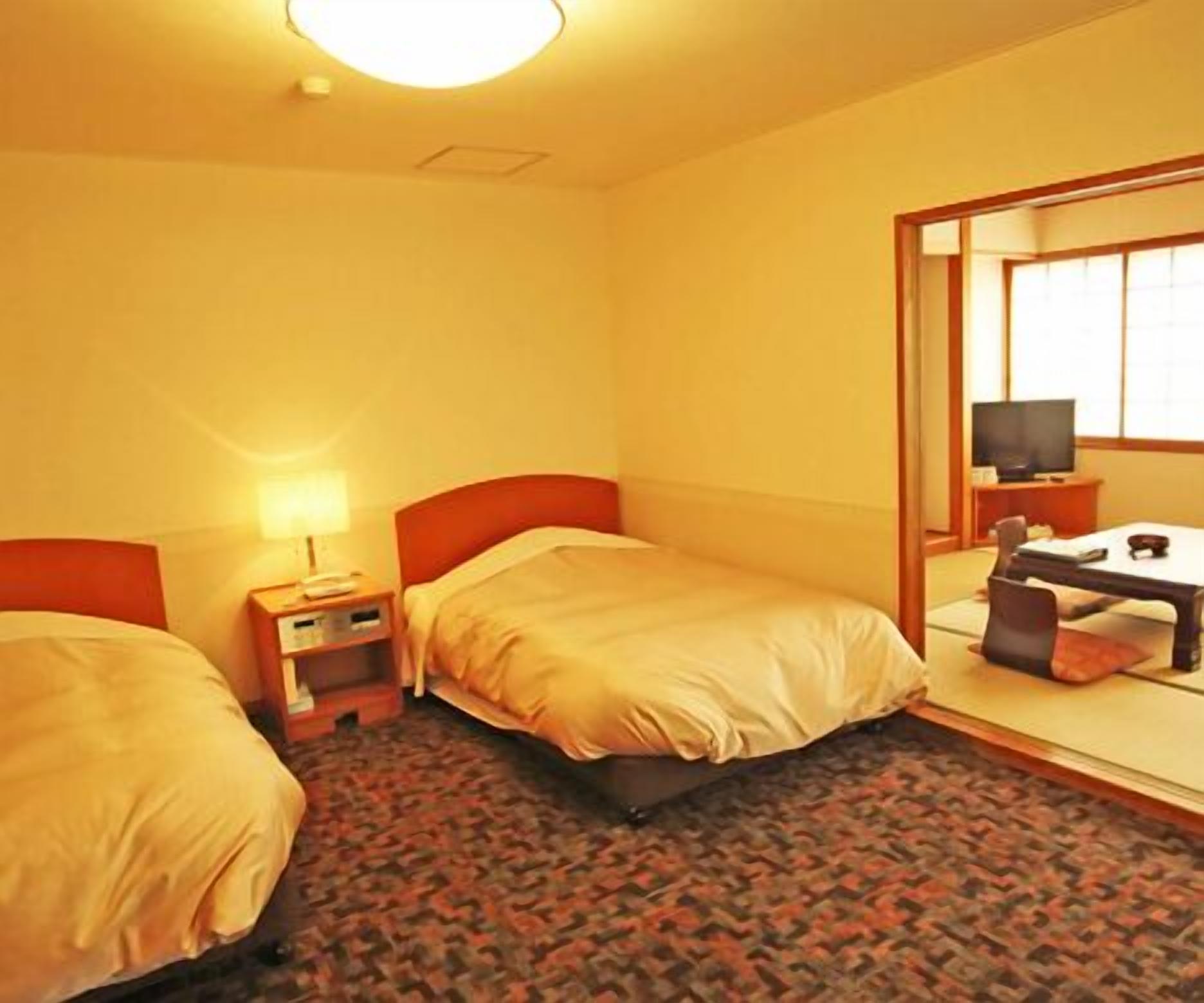 Una habitación de hotel con dos camas, un escritorio, una silla, un televisor y un espejo.