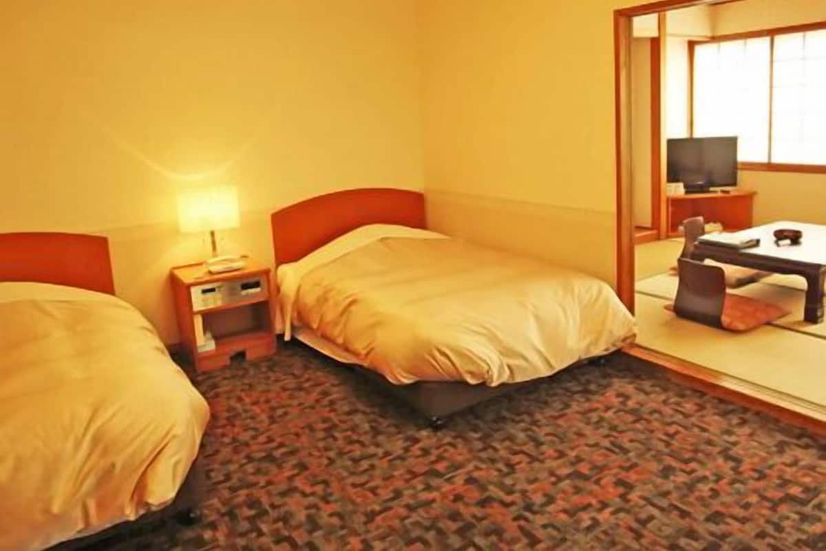 Una habitación de hotel con dos camas, un escritorio, una silla, un televisor y un espejo.