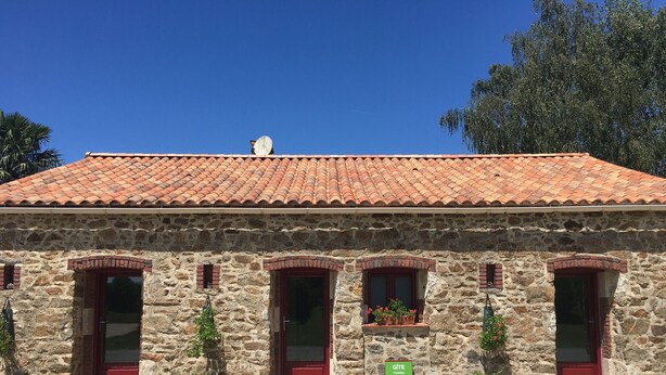 A stone building with a tiled roof, three windows with red frames, and a signboard in front. - Charming Cottage in Agricultural Hamlet, Near Puy du Fou, with Garden & BBQ (Saint-Michel-Mont-Mercure)
