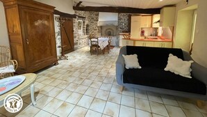 A spacious living area with a tiled floor, a wooden wardrobe, a dining table with chairs, a sofa, and a kitchen in the background. - Charming Cottage in Agricultural Hamlet, Near Puy du Fou, with Garden & BBQ (Saint-Michel-Mont-Mercure)