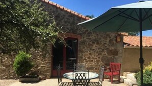 A stone building with a tiled roof, a patio with a table and chairs, and a green umbrella. - Charming Cottage in Agricultural Hamlet, Near Puy du Fou, with Garden & BBQ (Saint-Michel-Mont-Mercure)
