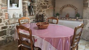 A stone-walled dining area with a round table covered by a checkered tablecloth, surrounded by wooden chairs. - Charming Cottage in Agricultural Hamlet, Near Puy du Fou, with Garden & BBQ (Saint-Michel-Mont-Mercure)