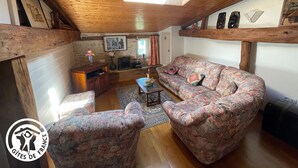 A cozy living room with wooden beams, a sofa, a coffee table, and a TV. - Charming Riverside House with Canoes, Garden, and Nearby Market in Marais Poitevin (Damvix)