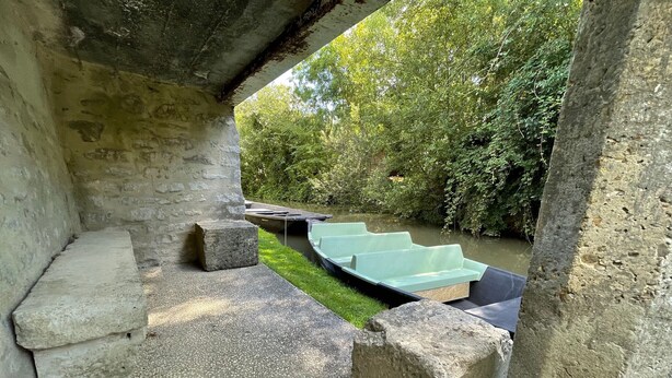 A stone bench area with steps leading to a boat on a river, surrounded by greenery. - Charming Riverside House with Canoes, Garden, and Nearby Market in Marais Poitevin (Damvix)