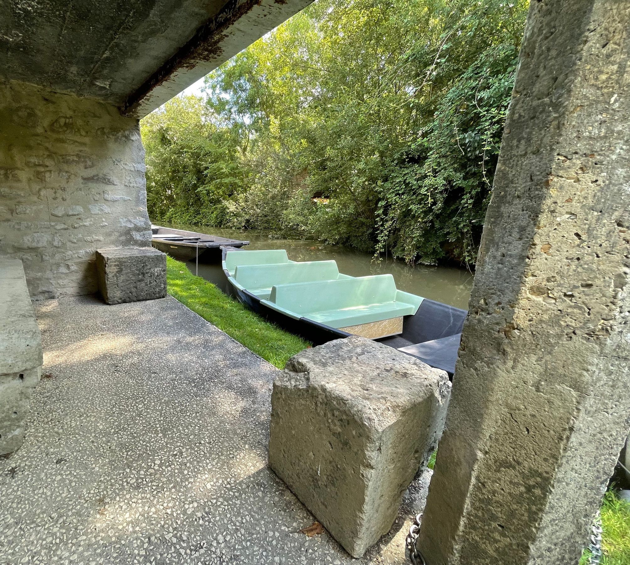 Un área con bancos de piedra y escalones que bajan hacia una barca en un río, rodeado de follaje.