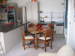 Compact kitchen with refrigerator, oven, and microwave, dining table, and white cabinet.