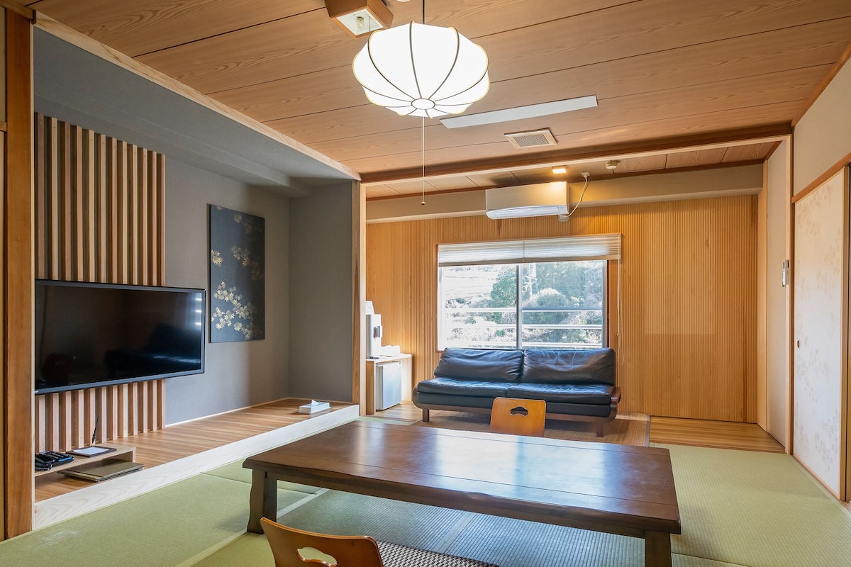A traditional Japanese room with tatami flooring, a low table, a sofa, a television, and a sliding door.
