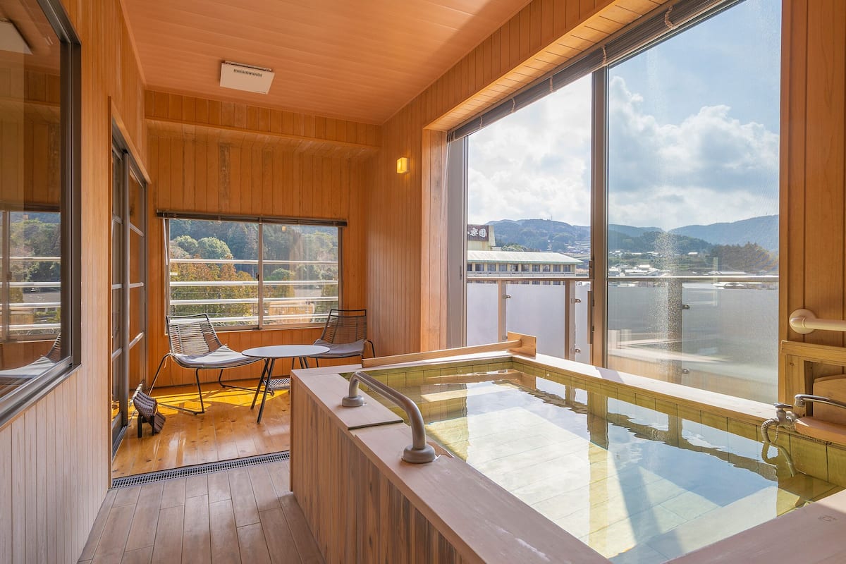 A wooden interior with a large window, a hot tub, and a view of a body of water.